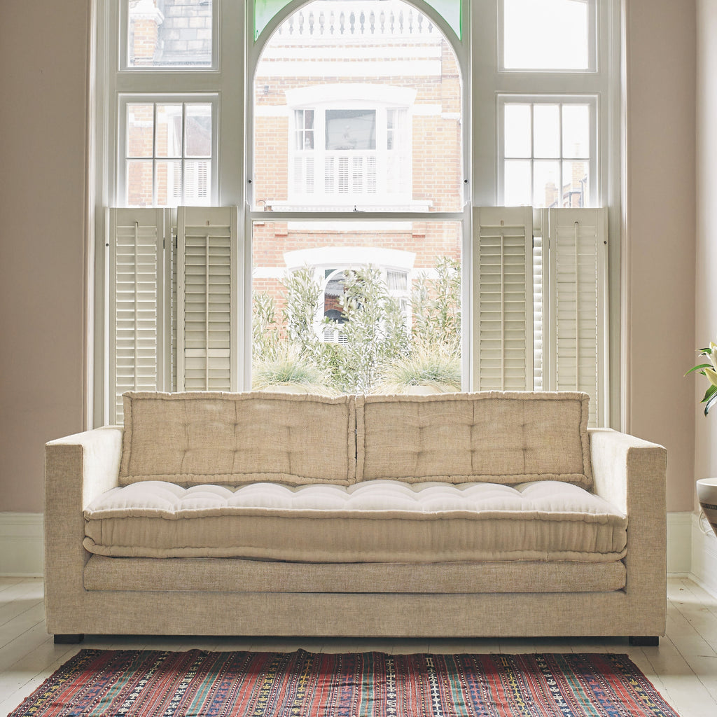 Martaba sofa in front of window, upholstered in plain light beige fabric.